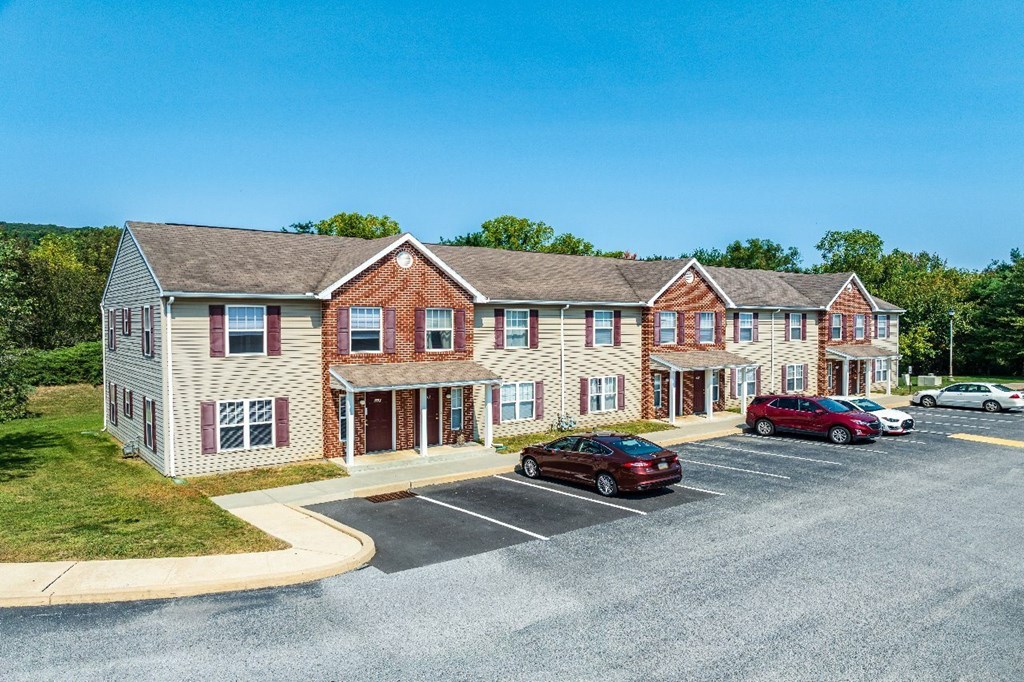 A parking lot in front of a two-story building with a red car parked in the lot.