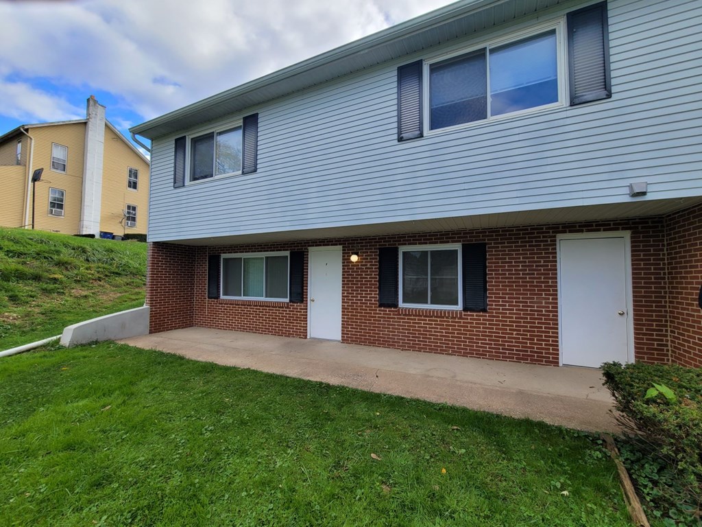 A house with a grey siding and a red brick base with a white door and windows.