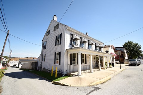 A white two-story house with a porch and a car parked in front.