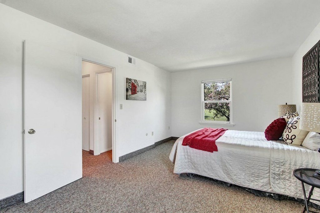 A bedroom with a bed, pillows, and a red blanket.