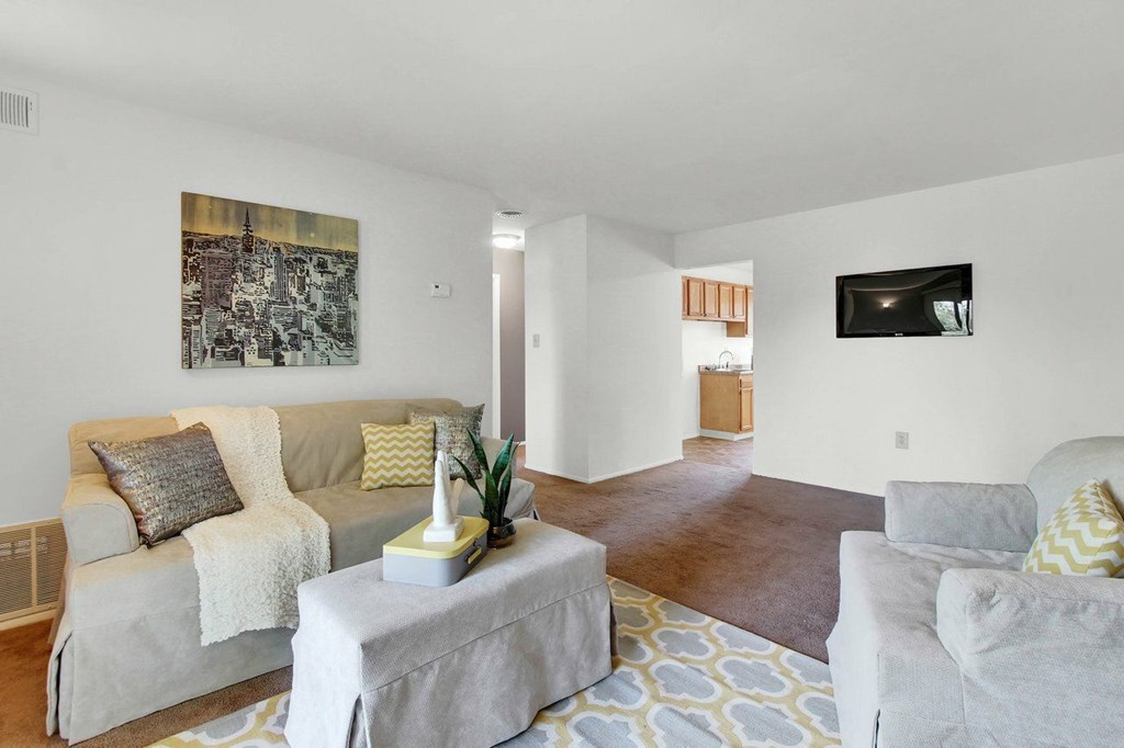 A living room with a grey couch, a white ottoman, and a painting on the wall.