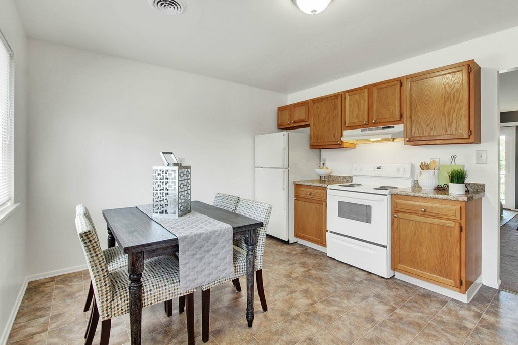 A kitchen with a table and chairs in the foreground and a refrigerator and oven in the background.