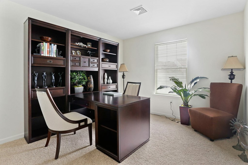 A brown desk with a chair and a bookshelf with various items on it.