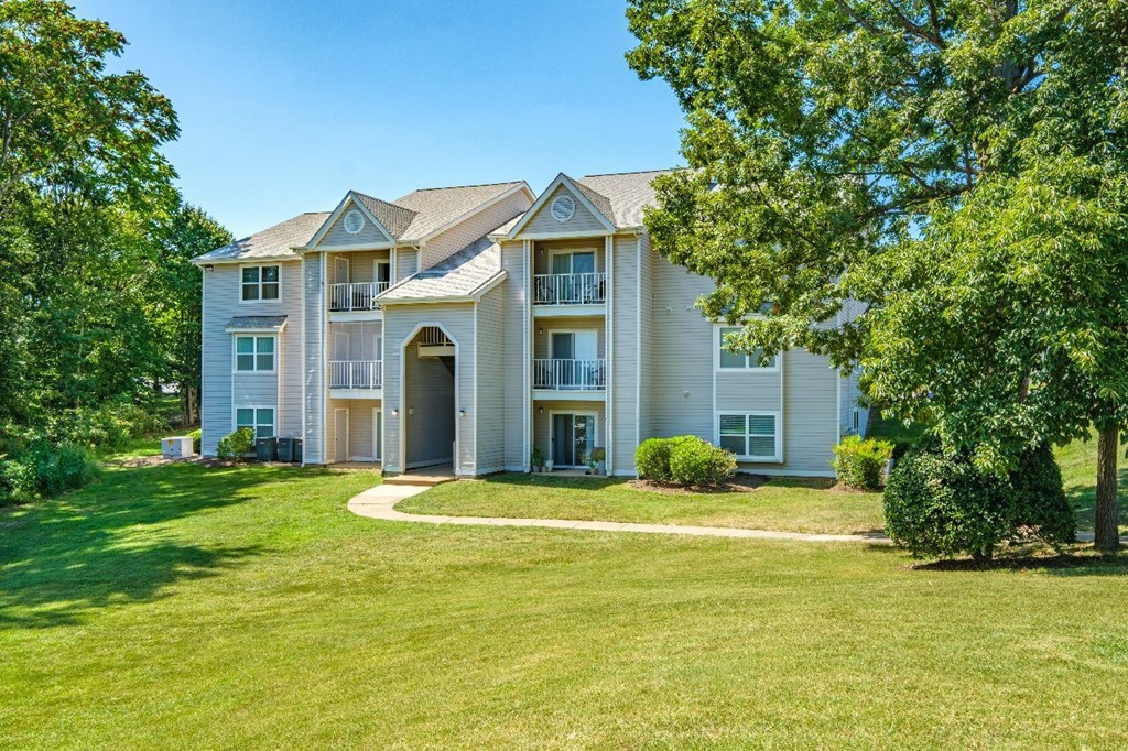 A large, well-maintained apartment complex with a green lawn and trees surrounding it.