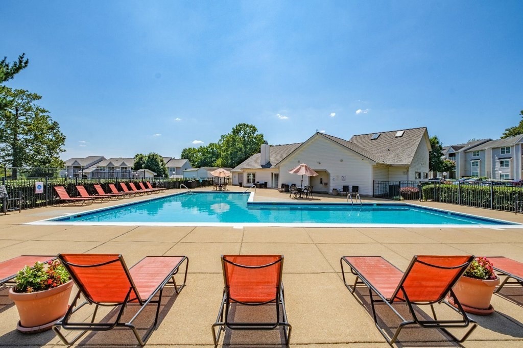 A pool surrounded by orange chairs and potted plants.
