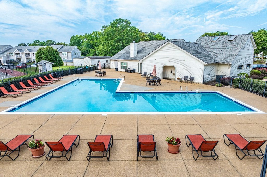 A pool surrounded by red lounge chairs and a white building in the background.