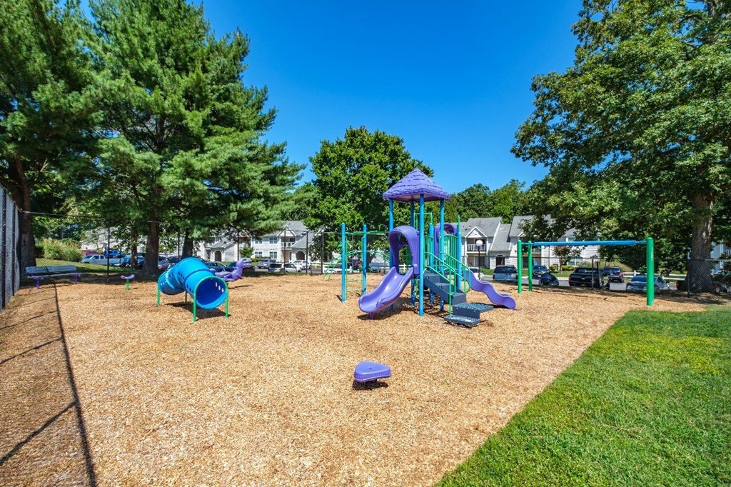 A playground with a purple and green slide and a blue and purple play structure.