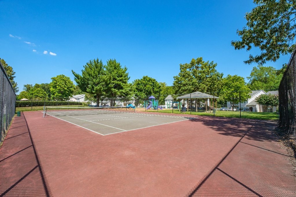 A tennis court surrounded by trees and a fence.
