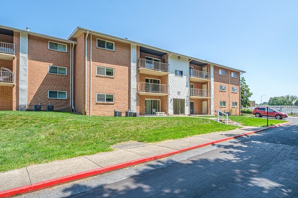 A red car is parked on the street in front of a brick apartment building.