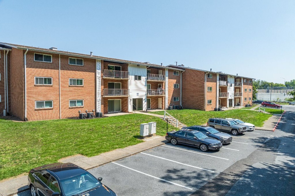 A row of apartment buildings with cars parked in front.