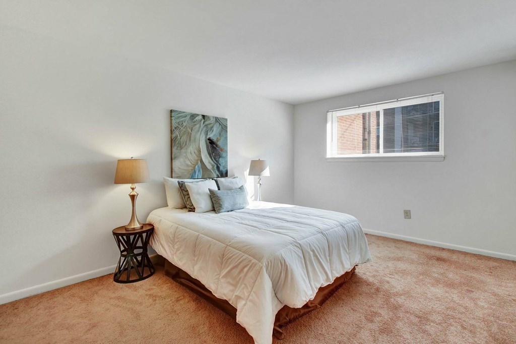 A bedroom with a bed, two lamps, and a painting on the wall.