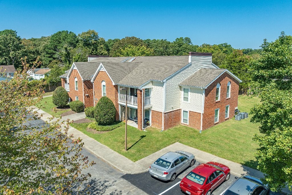 A red brick building with a white trim and a grey roof with a car parked in front.