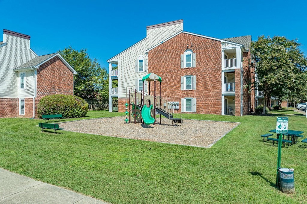 A playground with a green slide and a red brick building in the background.