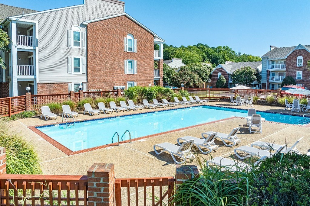 A pool surrounded by chairs and plants in front of a brick building.