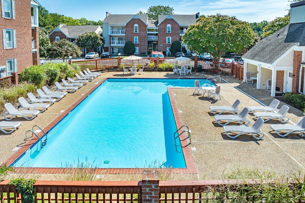 A large swimming pool surrounded by lawn chairs and trees.