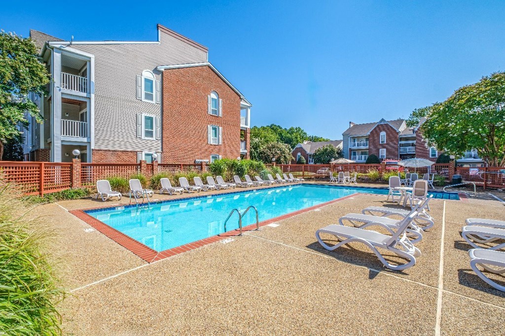 A pool surrounded by sun loungers and a brick building.