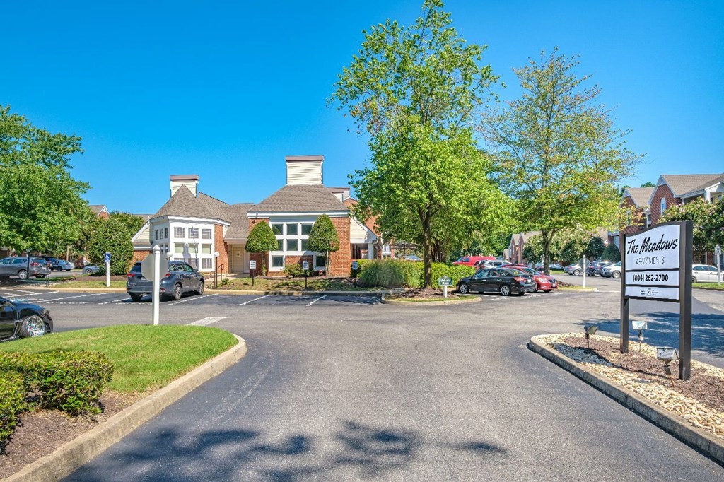 A sunny day at The Woodlands Apartments with cars parked and trees in the background.