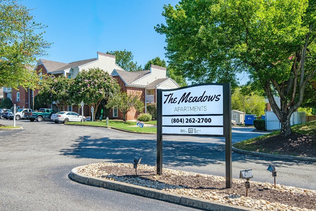 A sign for The Meadows Apartments stands in front of a parking lot.