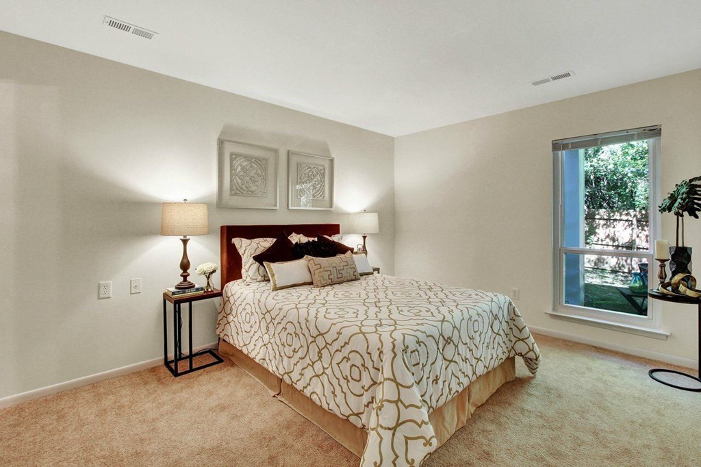 A bedroom with a bed, two lamps, and a window.