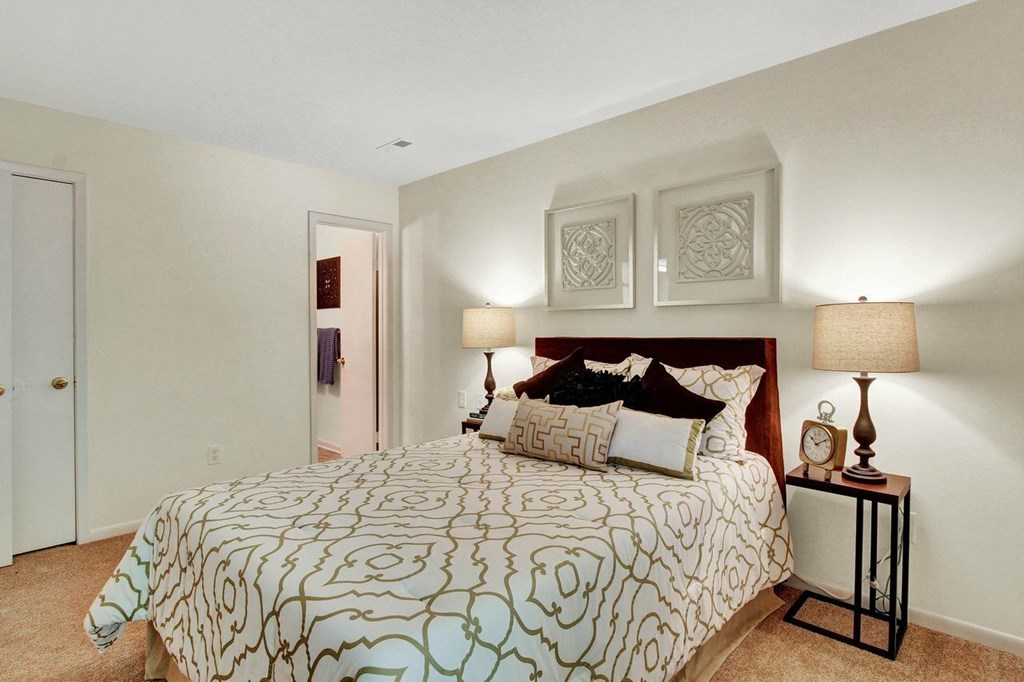 A bedroom with a patterned bedspread and two lamps on a side table.