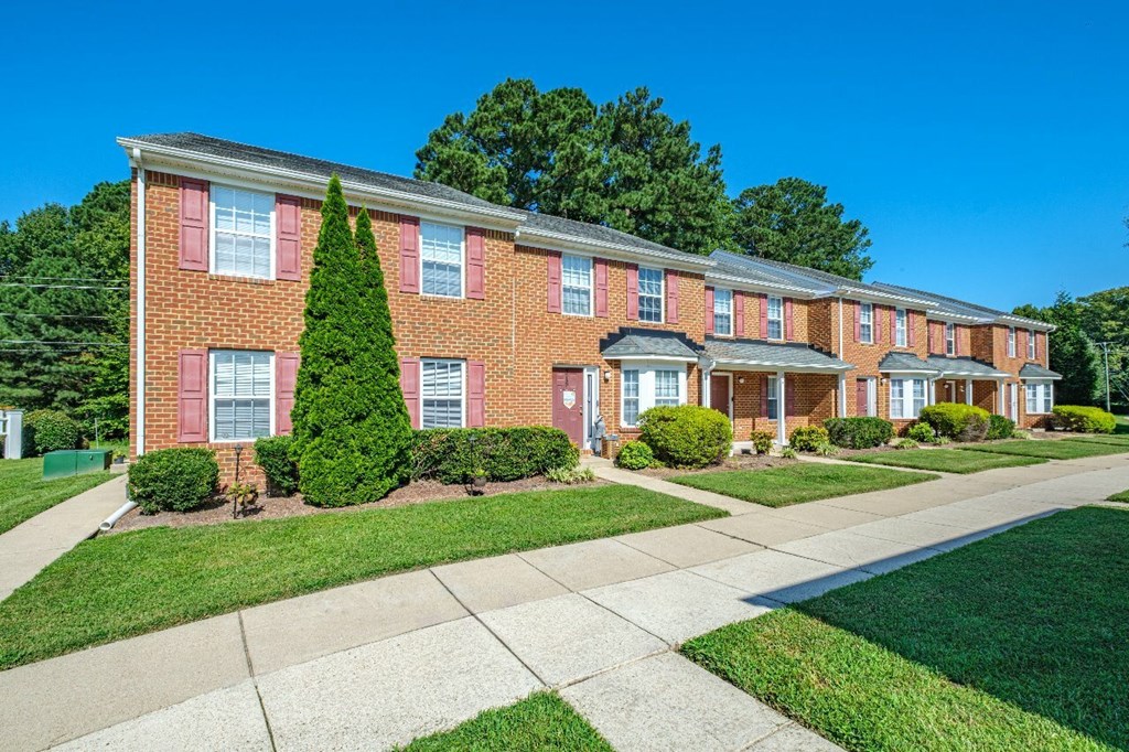 A red brick apartment building with green bushes in front.