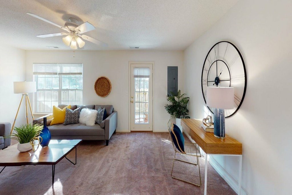 A living room with a grey couch, a wooden table, and a large clock on the wall.
