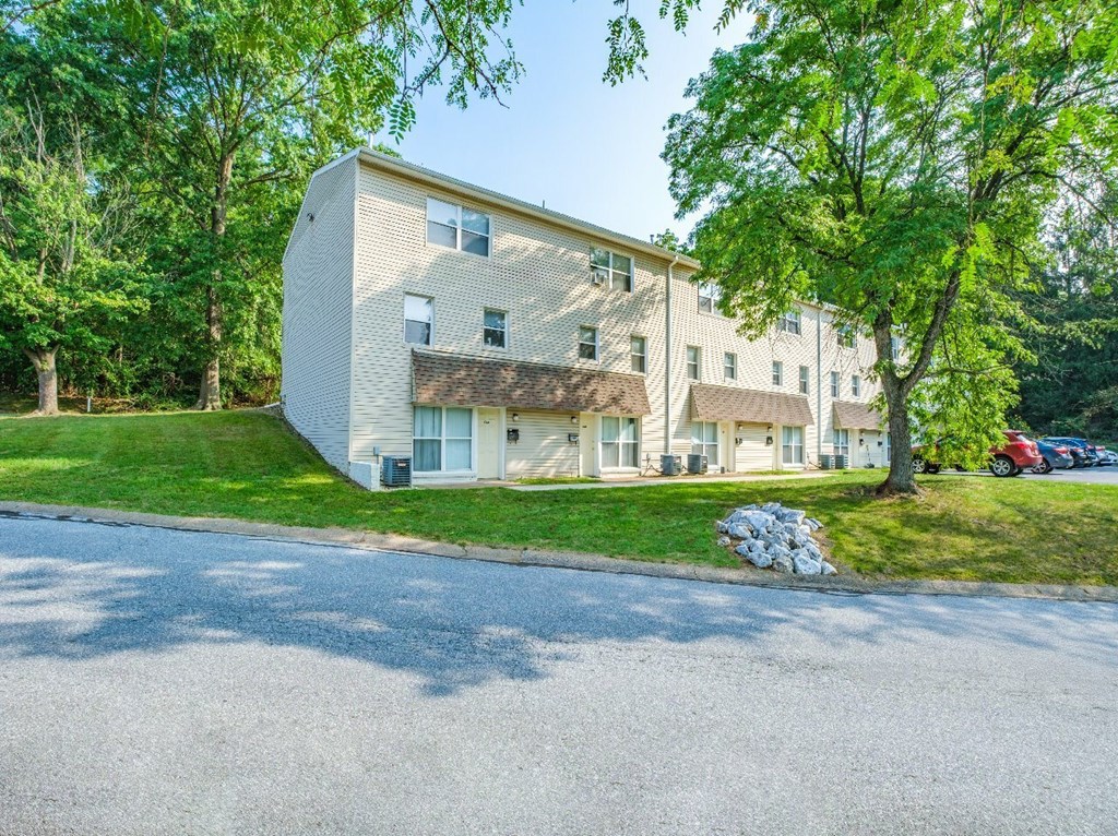 A two-story building with a grey and white exterior is surrounded by greenery.
