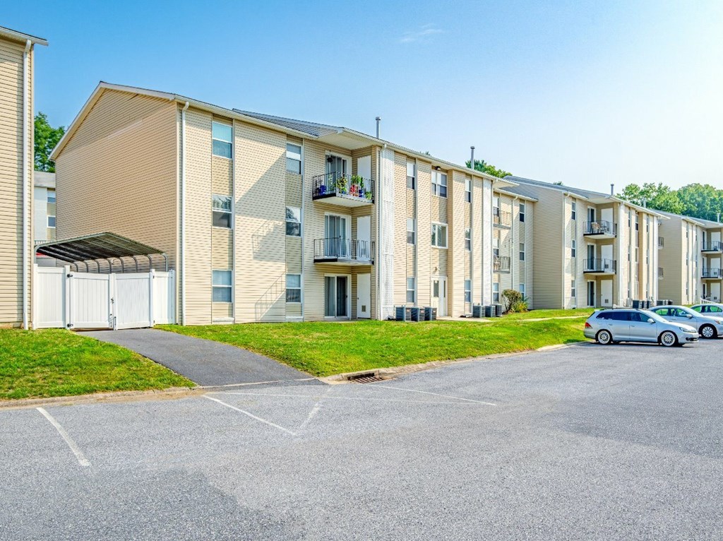 A row of apartment buildings with cars parked in front.
