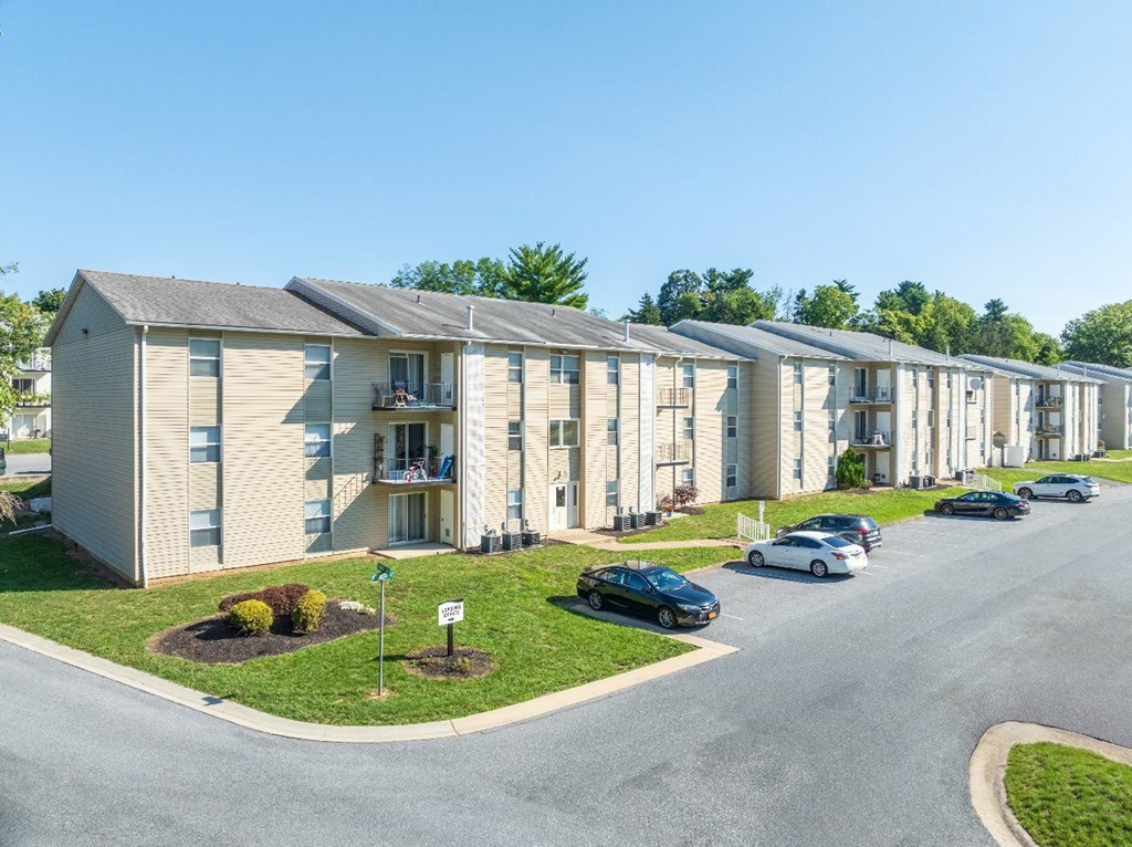 A row of apartment buildings with cars parked in front.