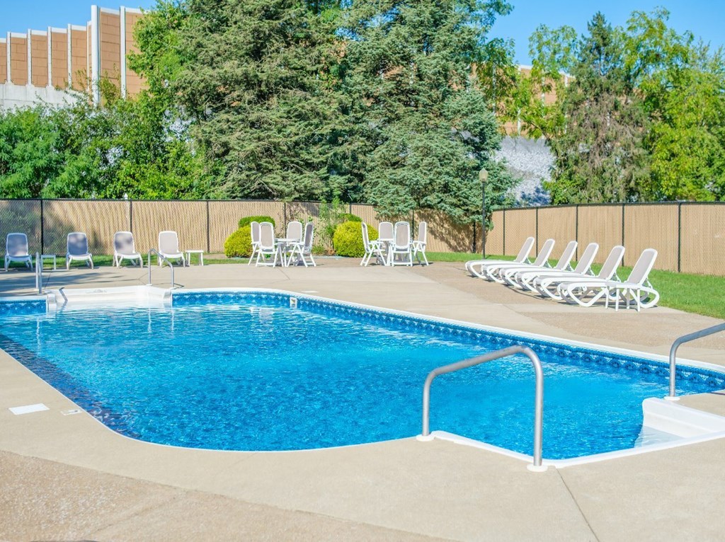 A blue swimming pool surrounded by white chairs and trees.