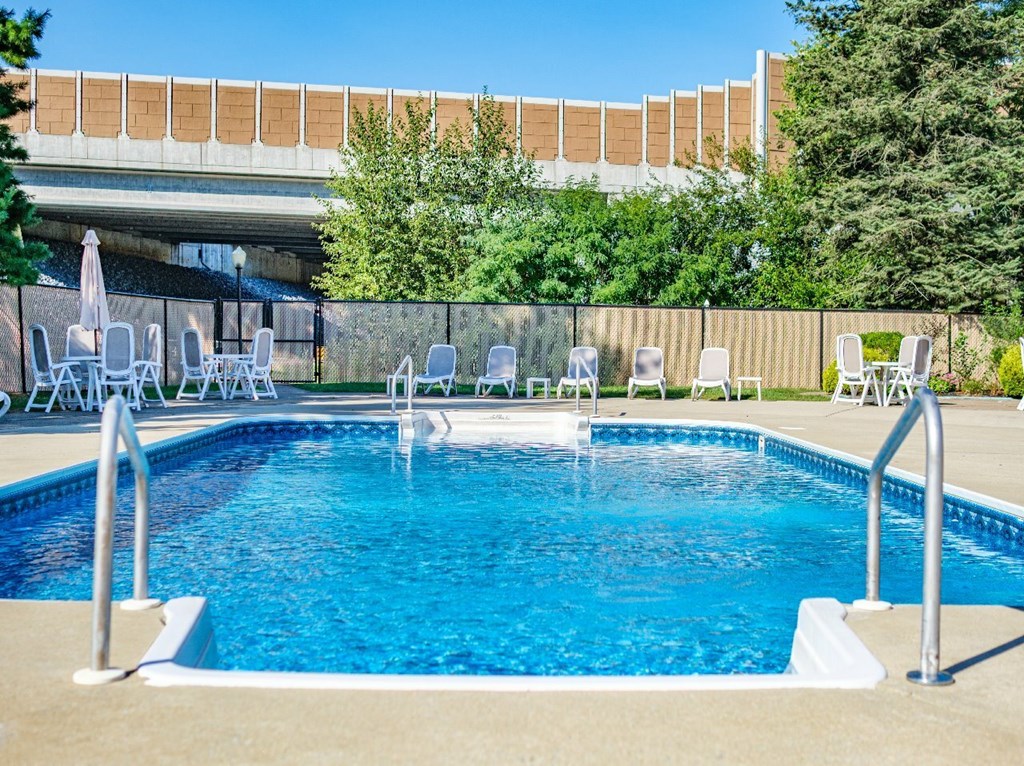 A pool with chairs around it and a building in the background.
