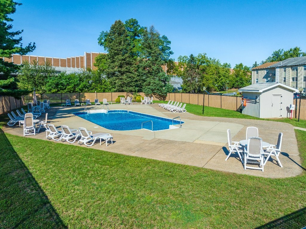 A pool with chairs around it and a building in the background.