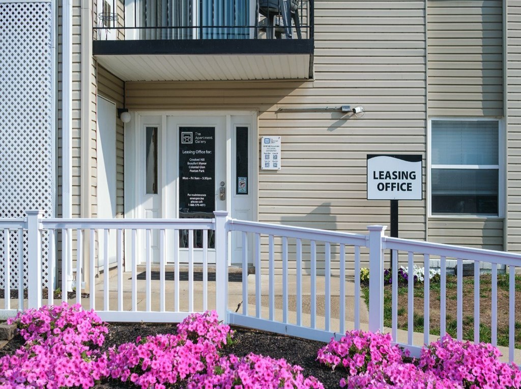 A building with a leasing office sign and a white fence with flowers in front.