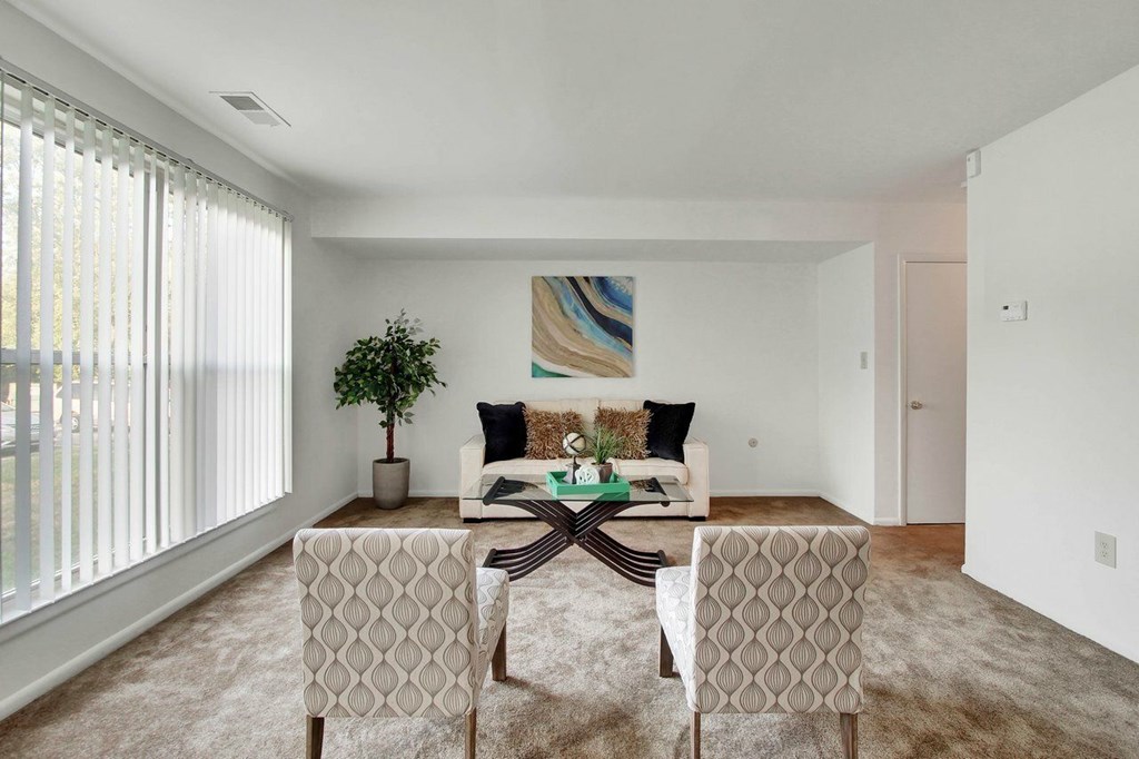 A living room with a white couch, a green plant, and a painting on the wall.