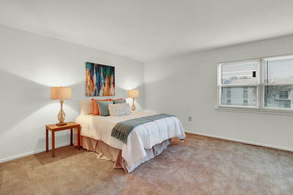 A bedroom with a bed, two lamps, and a painting on the wall.