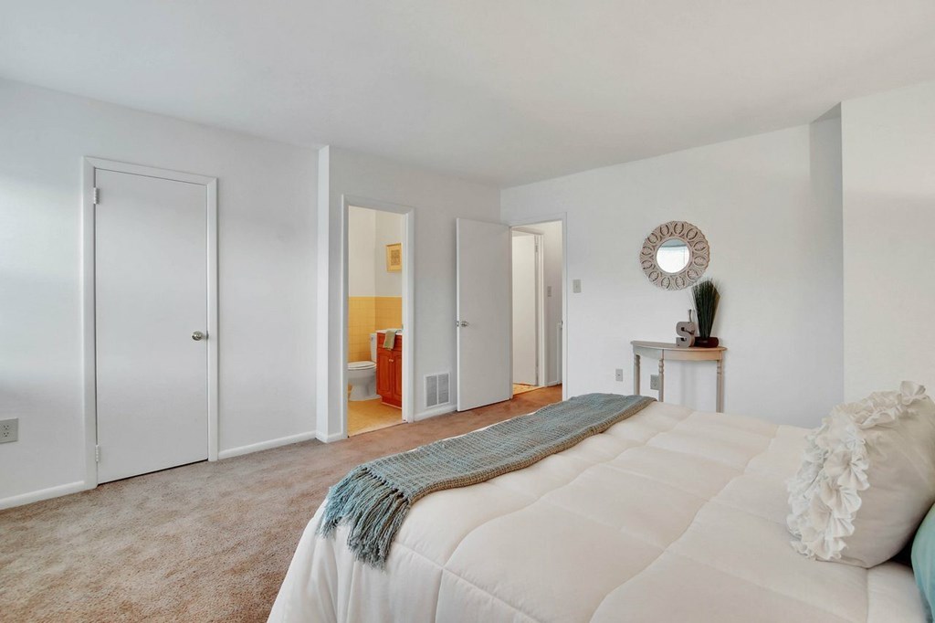 A bedroom with a bed, a mirror, and a small table with a plant on it.