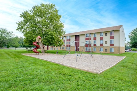 A playground with a slide and swings in front of a red and white building.