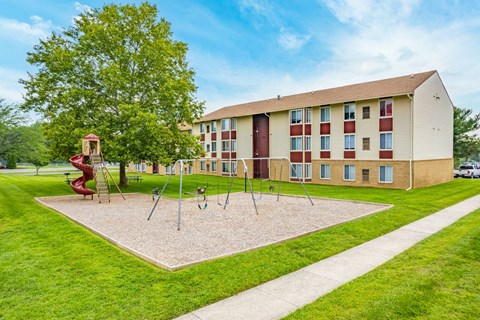 A playground with swings and slides is in front of a building.