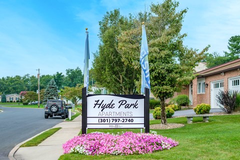 A sign for Hyde Park Apartments stands in front of a house with a blue sky in the background.