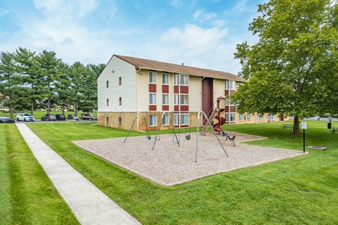 A playground with swings and a slide is in front of a two-story apartment building.