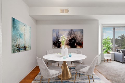 A dining room with a white table and chairs, a painting on the wall, and a view of the outdoors through the window.