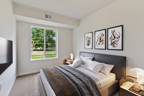 A bedroom with a large bed and a window overlooking a green lawn.