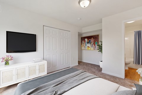 A white bedroom with a grey bedspread and a television on the wall.