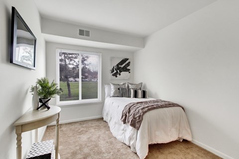 A bedroom with a bed, a table, a mirror, and a window with a view of trees.