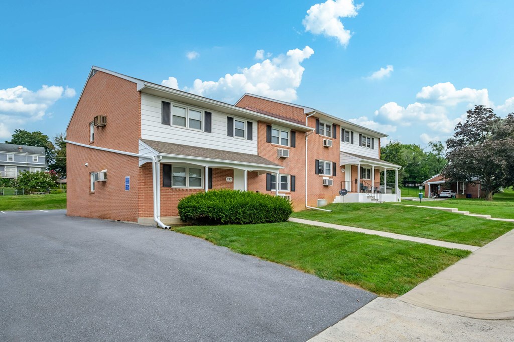 A red brick building with a white roof and a driveway in front.
