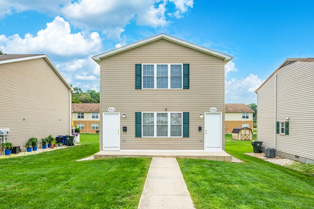 A beige house with green shutters and a white door is in the foreground with a clear blue sky above.