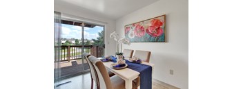 A dining room with a table set for two and a painting of flowers on the wall.