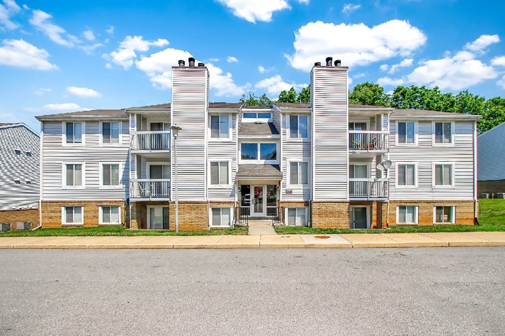 A large apartment building with multiple balconies and a parking lot in front.