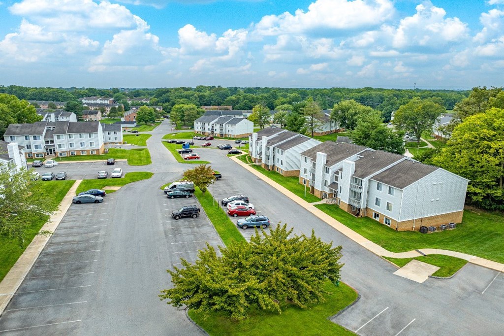 A road with cars parked on the side and houses in the background.