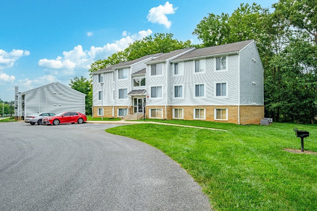 A red car is parked in front of a grey building.